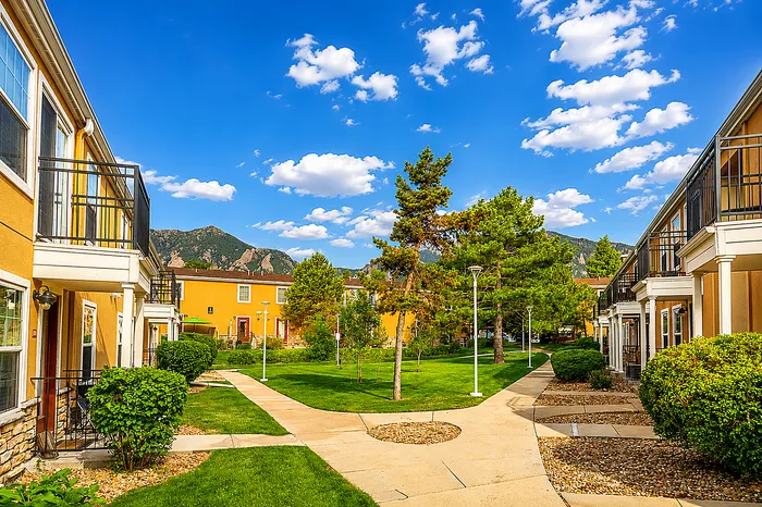 Beautiful apartment courtyard with lush greenery and scenic mountain views, surrounded by charming townhomes under a bright blue sky.
