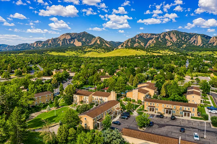 Charming residential community nestled amidst lush greenery with stunning mountain views, under a vibrant blue sky.