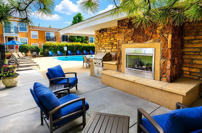 Charming outdoor space with cozy blue seating, a stone fireplace, and poolside view, perfect for relaxing or entertaining.