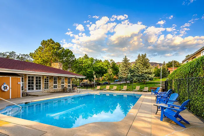 Charming outdoor pool area with inviting blue chairs, surrounded by lush greenery and picturesque mountain views.