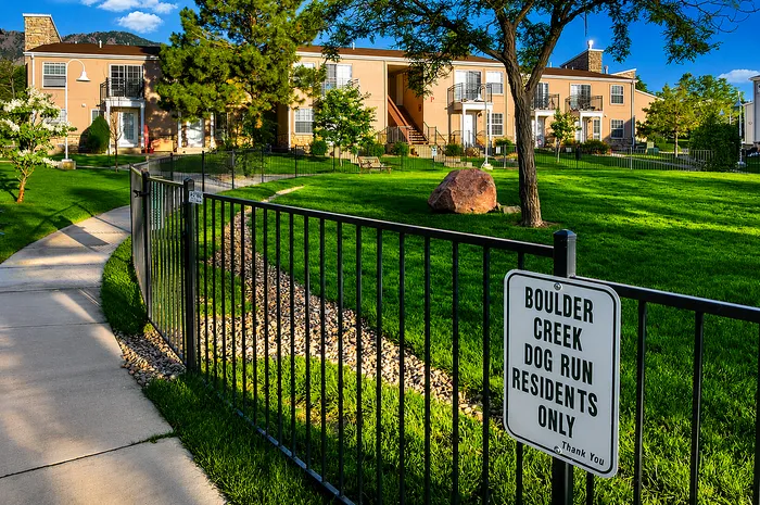 Charming apartment building surrounded by lush greenery and a private dog run in a serene neighborhood setting.