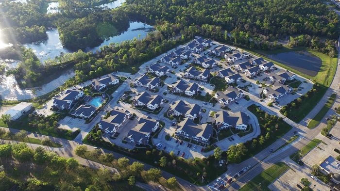 Aerial view of a serene apartment community surrounded by lush greenery and sparkling water features, showcasing modern villas with immaculate landscaping.