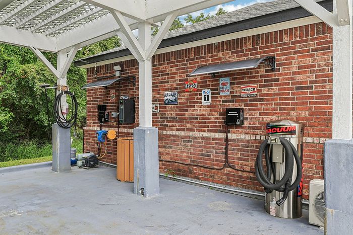 Charming outdoor car wash station with vintage-inspired signage, featuring a brick wall backdrop, convenient vacuum, and washing equipment under a stylish pergola roof.