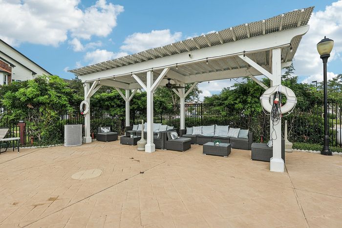 Charming outdoor lounge area with cozy seating under a stylish pergola, surrounded by lush greenery and a clear blue sky.