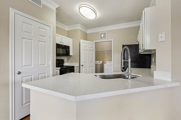 Modern kitchen with sleek white countertops, stainless steel fixtures, and integrated laundry area.