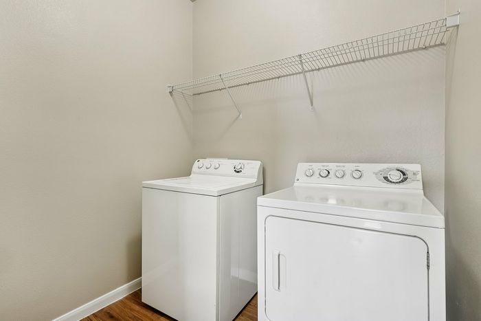 Modern laundry room featuring sleek white washer and dryer with convenient shelving above, offering functionality in a compact space.
