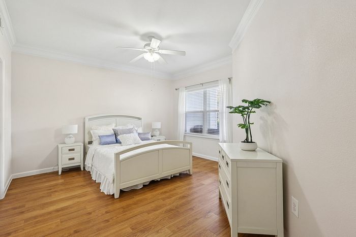 Bright and airy bedroom with elegant hardwood floors, featuring a cozy bed, sleek dresser, and natural light pouring through a large window.