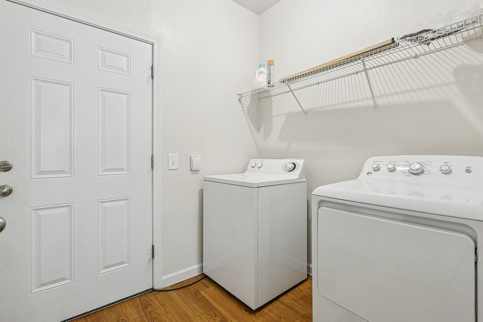 Bright, efficient laundry room with modern washer and dryer, featuring convenient shelving and stylish wood flooring.
