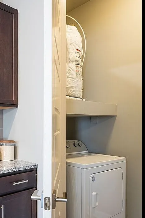 Chic apartment kitchen with elegant dark cabinetry, sleek granite countertops, and modern appliances, featuring a convenient adjacent laundry room with stacked washer and dryer.