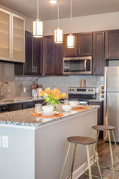 Modern kitchen with elegant granite countertops, stylish bar stools, stainless steel appliances, and warm pendant lighting.