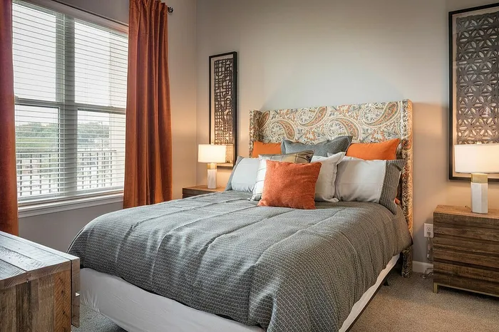 Cozy bedroom showcasing a stylish patterned headboard, warm orange accents, and elegant wooden furniture.