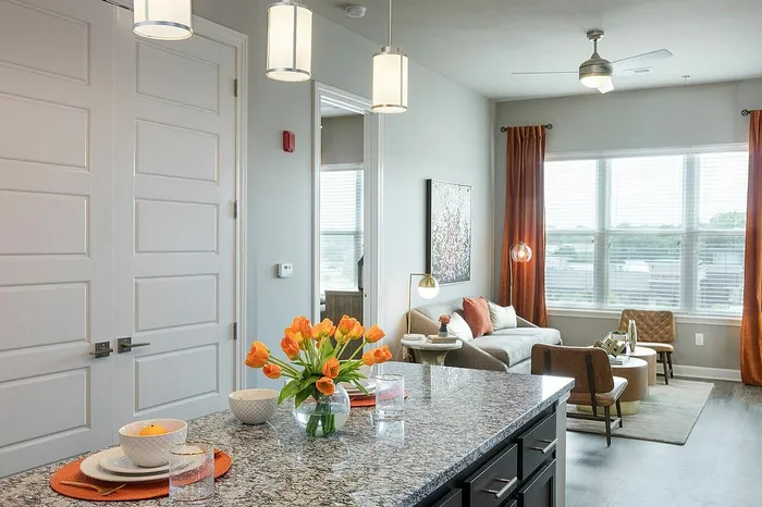 Chic modern living area with granite kitchen island, vibrant tulip centerpiece, and cozy seating by large sunlit windows.