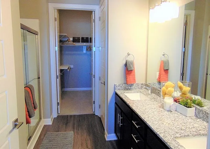 Elegant bathroom with granite countertop, double sinks, glass shower, and attached walk-in closet.