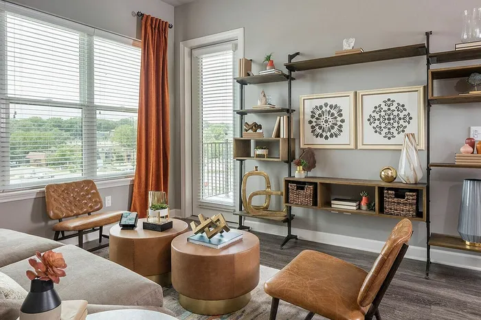 Chic living room with stylish shelving, modern art, and cozy seating bathed in natural light from large windows.