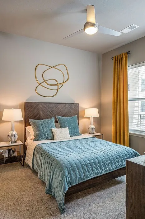 Chic bedroom with modern decor, featuring a plush blue comforter, stylish wall art, and bright natural light from large windows.