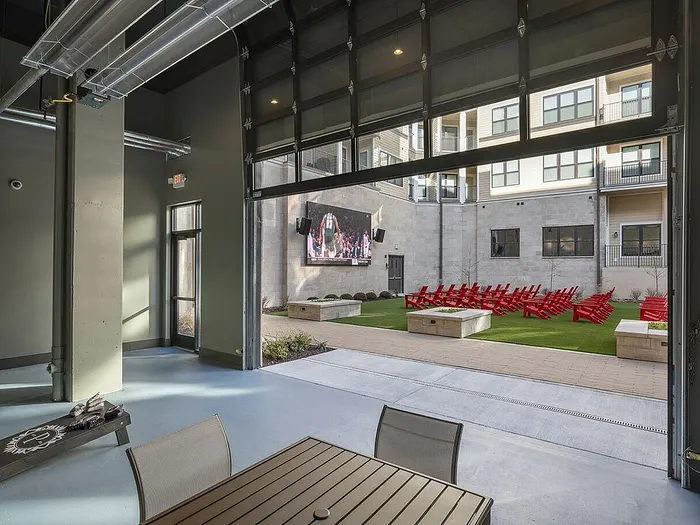 Modern apartment courtyard with red lounge chairs, large screen outdoor entertainment, and spacious seating area.