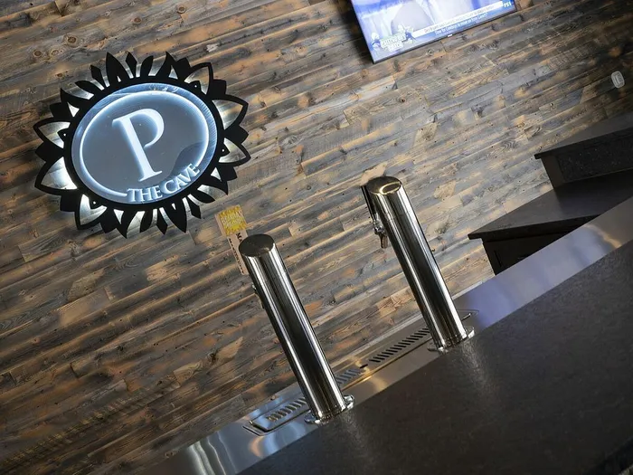 Chic bar with sleek taps and a rustic wood-paneled backdrop, featuring a stylish illuminated 'P The Cave' sign.