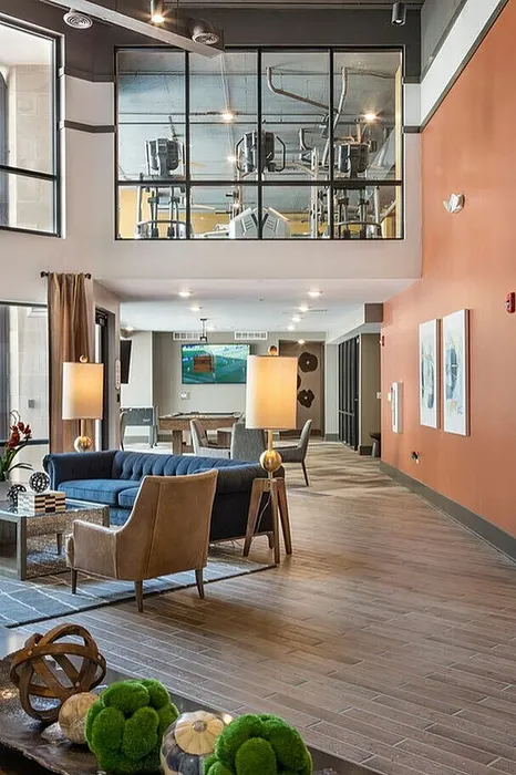 Elegant open-concept lounge with modern decor and gym view, featuring stylish seating and warm lighting.
