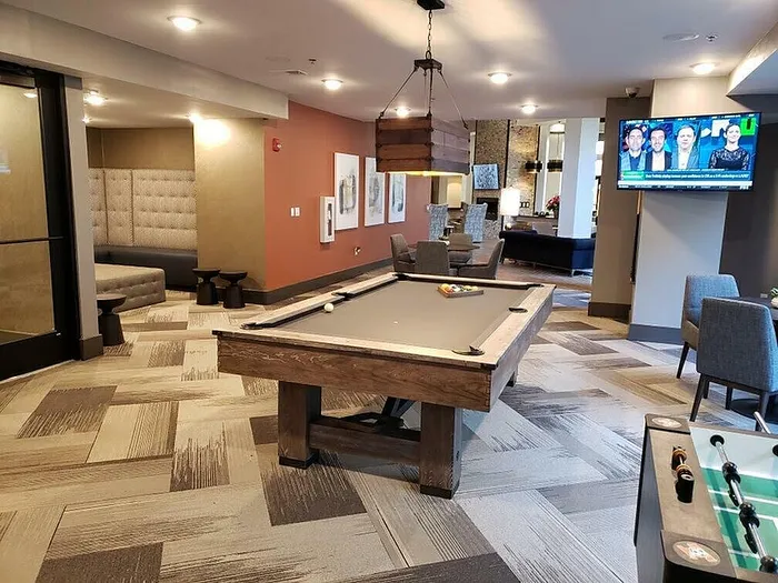 Elegant apartment recreation room featuring a chic pool table, cozy seating area, and flat-screen TV, perfect for entertainment and relaxation.