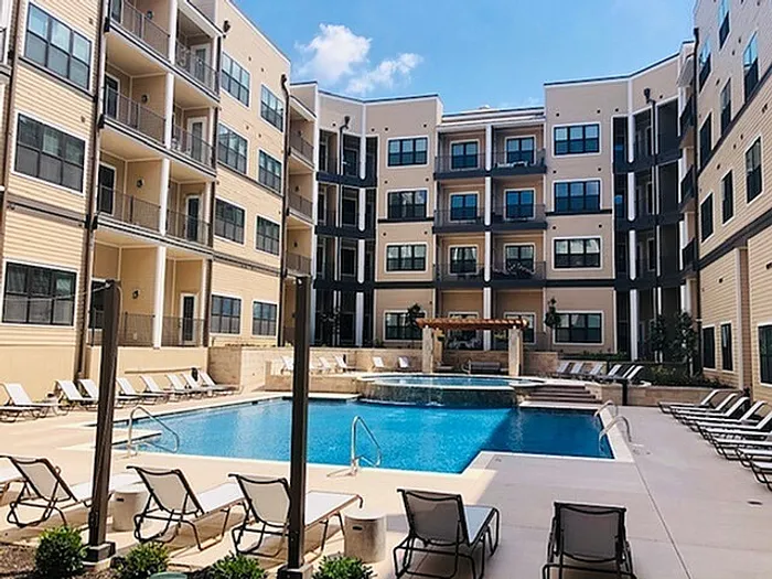 Modern apartment complex with inviting pool area, surrounded by stylish balconies and sun loungers under a clear blue sky.
