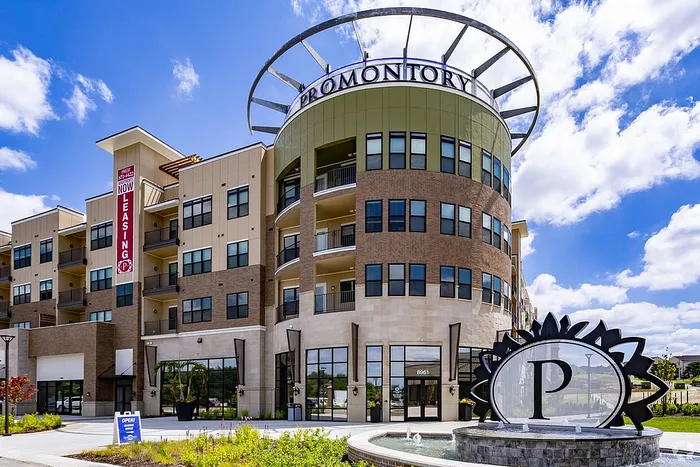 Modern apartment building exterior at Promontory with elegant architectural design, featuring large windows and vibrant landscaping, under a bright blue sky.