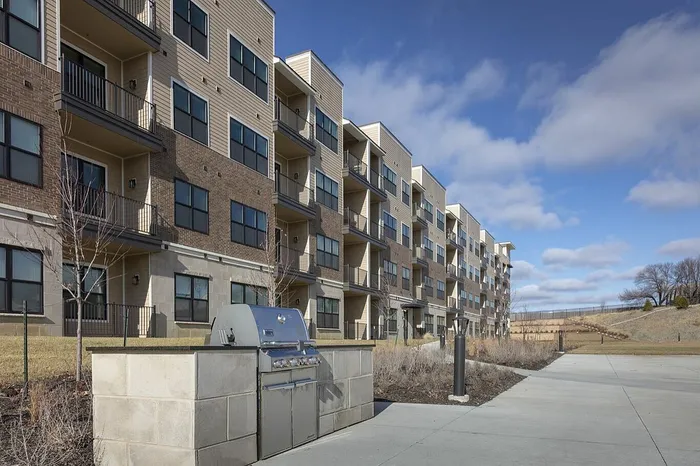 Modern apartment complex with spacious balconies, outdoor grill area, and scenic surroundings under a clear blue sky.