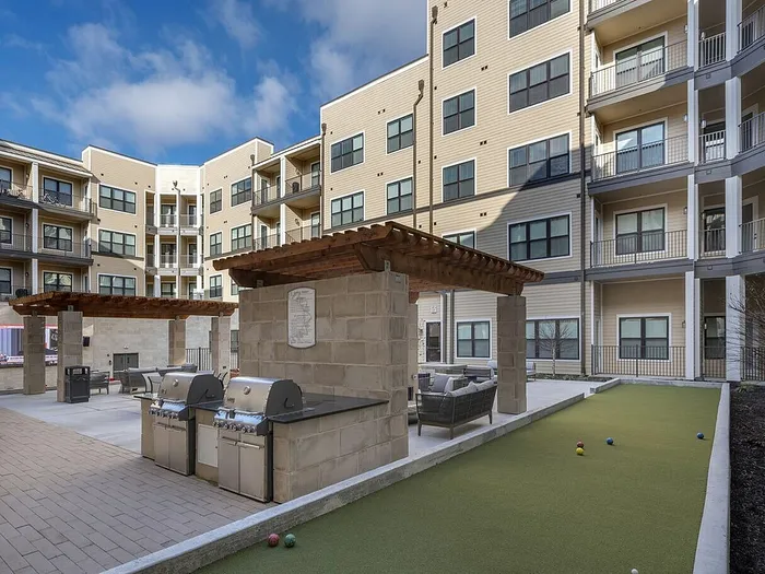 Modern apartment courtyard featuring outdoor grills, comfortable seating under pergolas, and a well-maintained bocce ball court.