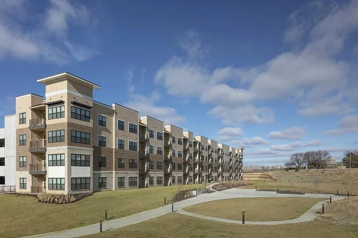 Modern multi-story apartment complex with expansive green lawns and clear blue skies.