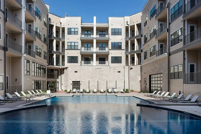 Luxurious apartment complex featuring a pristine swimming pool surrounded by stylish lounge chairs, perfect for relaxation and leisure.