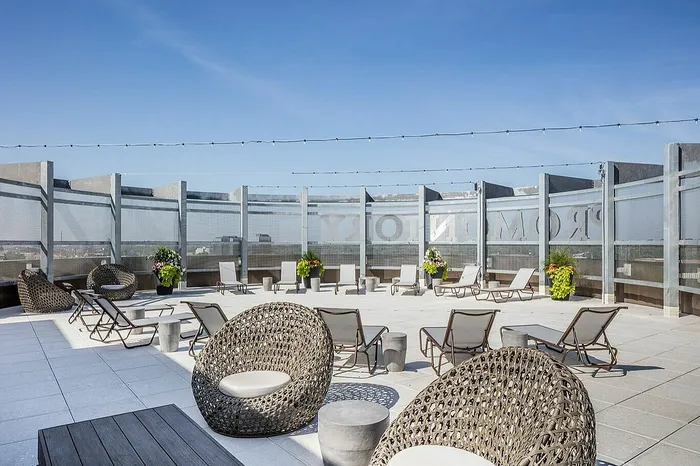 Luxurious rooftop terrace with modern wicker seating, sun loungers, and potted greenery under a clear blue sky.