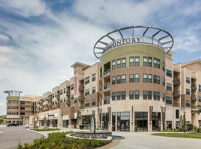 Modern apartment complex with sleek architectural design and spacious balconies, featuring a prominent entrance and lush landscaping.