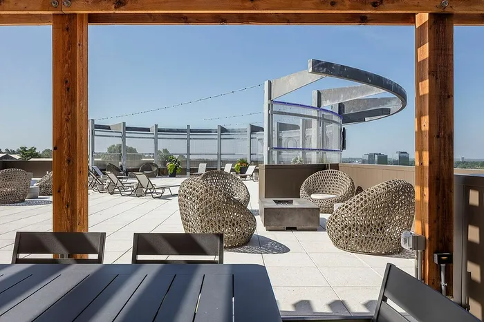 Modern rooftop terrace featuring stylish wicker furniture, lounge chairs, and panoramic city views.