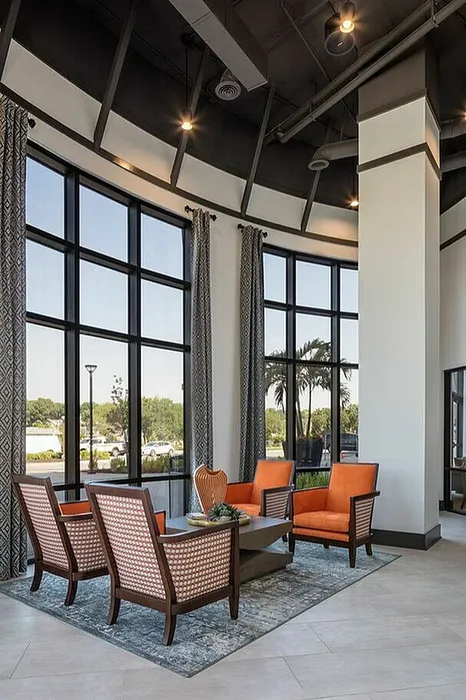 Luxurious living area with high ceilings, expansive windows, and elegant orange and wicker furniture offering a scenic outdoor view.