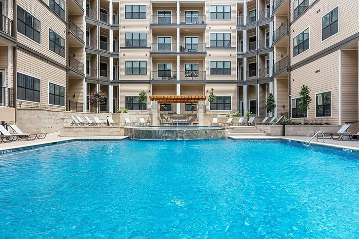 Luxurious apartment complex featuring a stunning pool, elegant architecture, and relaxing poolside lounge chairs.