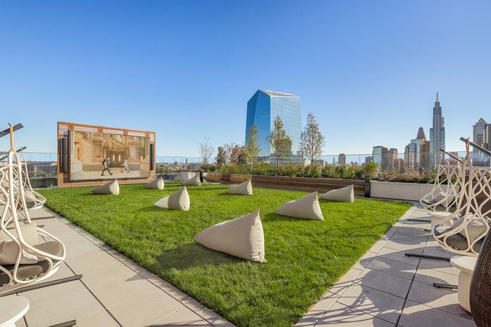 Chic rooftop terrace with plush seating, lush green lawn, and a large outdoor screen offering stunning city skyline views.