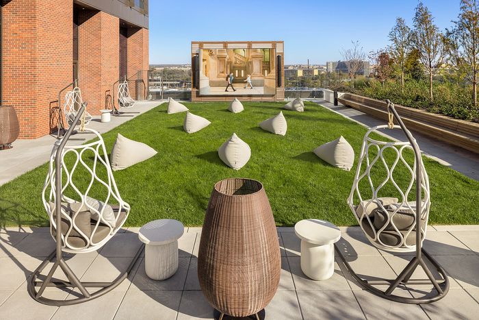 Chic rooftop lounge featuring stylish hanging chairs, modern patio seating, and vibrant green lawn with city views, perfect for relaxation and social gatherings.