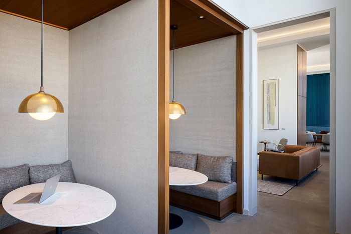 Modern apartment interior featuring cozy alcove seating with round tables under stylish pendant lights, adjacent to a chic lounge area with contemporary furniture and artwork.