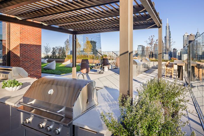 Stunning rooftop patio with modern grill area and lush greenery, offering breathtaking city skyline views.