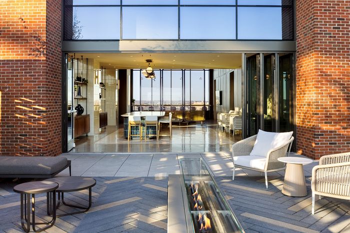 Stunning modern indoor-outdoor living space featuring sleek glass doors, cozy seating, and an elegant fire pit with city views.