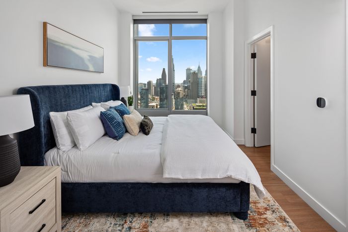 Luxurious bedroom with a plush velvet bed and skyline view, featuring elegant decor and large window for natural light.
