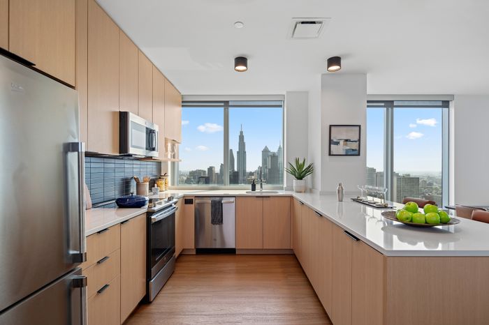 Modern kitchen with sleek cabinetry, stainless steel appliances, and stunning city skyline view through large windows.