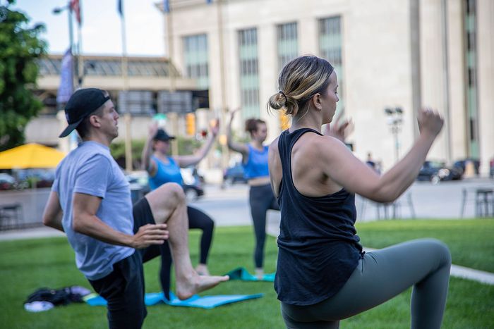 Vibrant outdoor fitness class with diverse group exercising together on green lawn in the city.