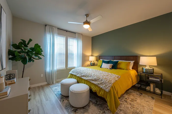 Inviting bedroom featuring a plush yellow bed, a stylish ceiling fan, and cozy lighting, accented by chic decor and natural elements.