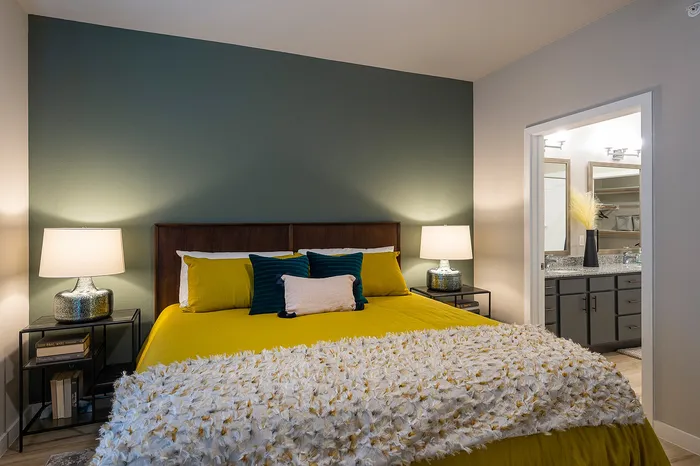 Elegant bedroom with a cozy ambiance featuring a plush yellow bedspread, stylish lighting, and a glimpse into a modern bathroom suite.
