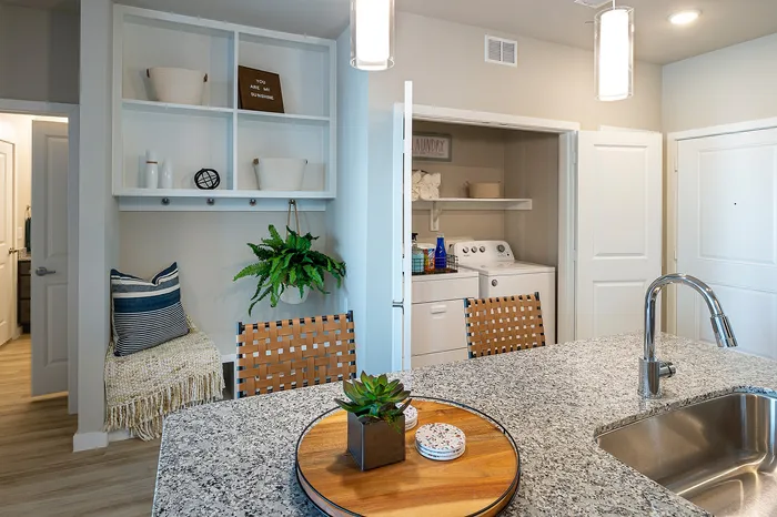 Modern apartment interior showcasing a sleek laundry area, stylish open shelving, and a chic granite kitchen island with a contemporary faucet.