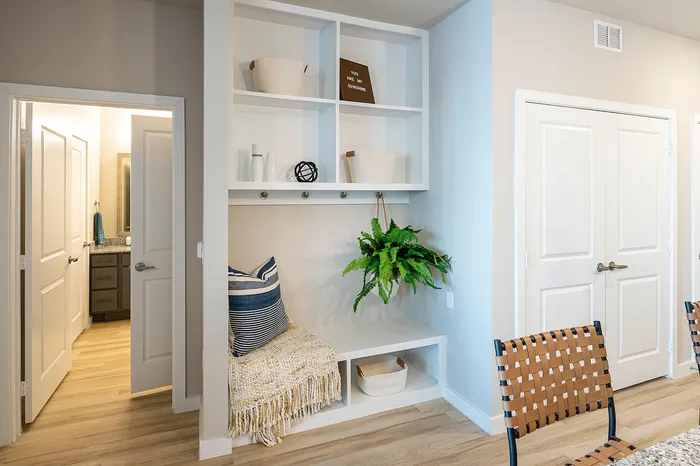 Charming apartment nook with modern shelving, cozy seating, and vibrant greenery, adjacent to a sleek bathroom with stylish cabinetry.