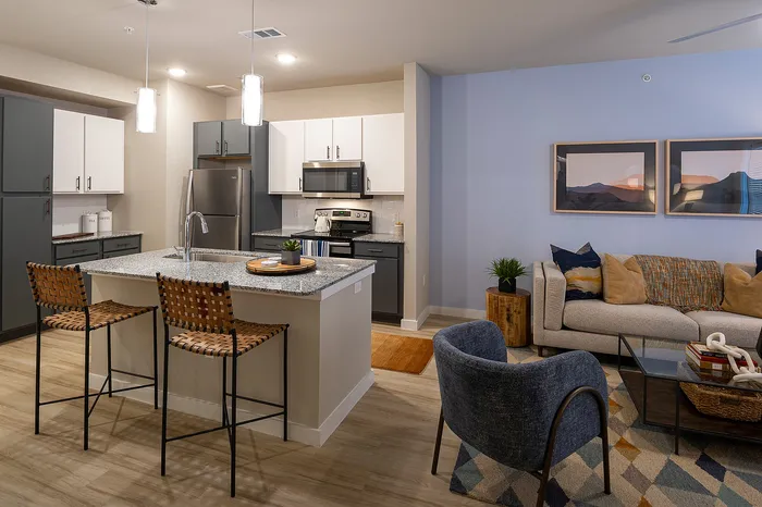Modern open-plan kitchen and living room with stylish decor, featuring a cozy seating area, elegant lighting, and a sleek kitchen island with wicker bar stools.