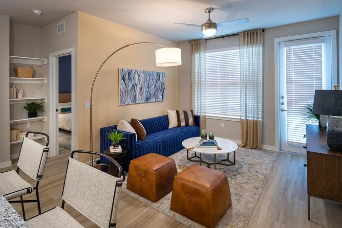 Chic living room featuring a blue velvet sofa, modern decor, and natural light through large windows.