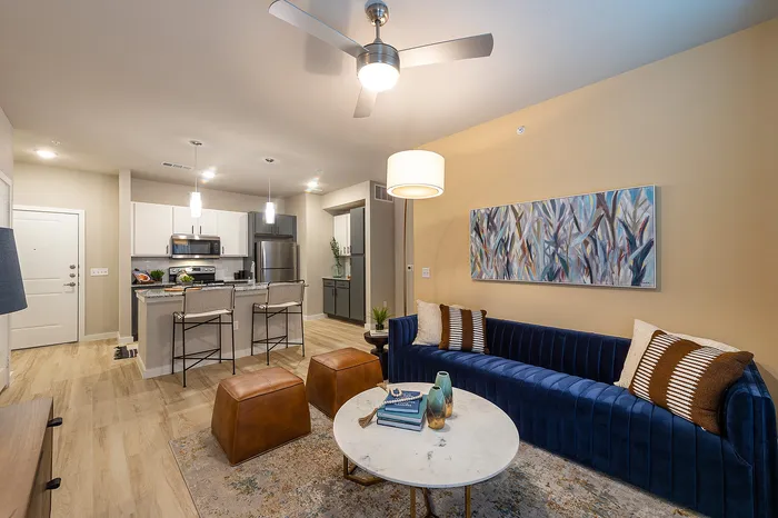 Modern open-plan living area featuring a stylish kitchen with stainless steel appliances, elegant pendant lighting, and a cozy living room with a plush blue sofa and chic decor.