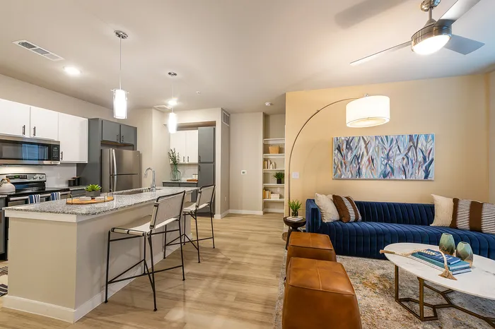 Modern apartment interior with a sleek kitchen island, stylish blue sofa, and contemporary decor in an open-concept living space.